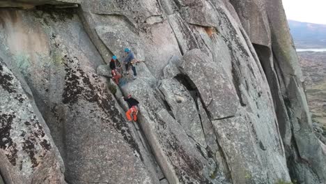 Tres-Escaladores-Ascendiendo-Por-Una-Pared-De-Granito,-Con-Un-Lago-Al-Fondo