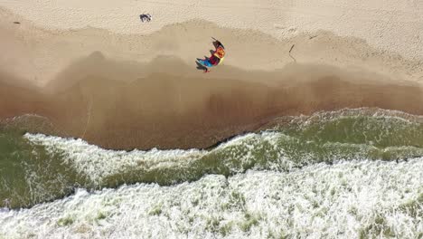 Antenne:-Draufsicht-Eines-Surfers,-Der-Zu-Seinem-Winddrachen-Kommt,-Der-An-Einem-Sandstrand-In-Nida-Platziert-Ist