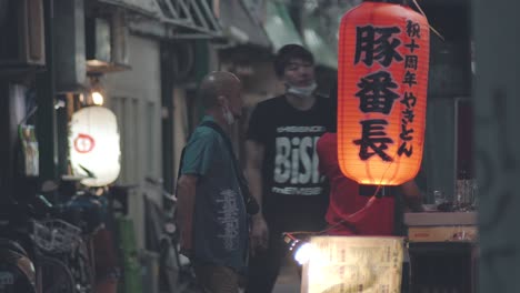 Japoneses-Charlando-Con-Sus-Máscaras-Tiradas-Debajo-Del-Cuello-Frente-A-Un-Restaurante-En-Kamata,-Tokio,-Japón