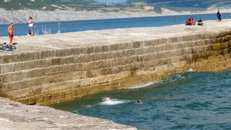 A-boy-cannonballs-off-of-a-stone-pier-into-a-rough-sea-on-a-summers-day