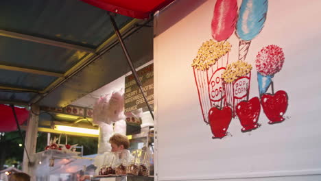 Mother-and-daughter-buying-cotton-candy-from-carnival-food-vendor,-Tilt-Down,-Pan-Left,-Slow-Motion