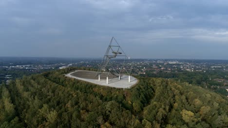 Pair-jogs-underneath-the-Tetraeder-landmark,-wide-drone-tracking-shot