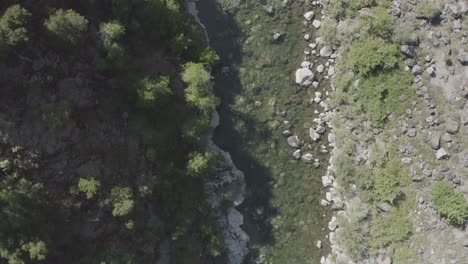 Slow-drone-flight-over-a-rocky-river-surrounded-by-greenery