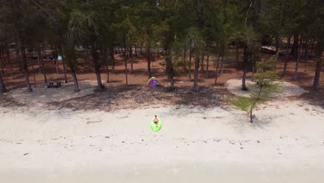 Tiro-De-Dron-Del-Hombre-Acostado-En-El-Sofá-De-Aire-Verde-En-La-Playa-De-Arena-Con-Tienda-Detrás