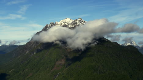 Hermosa-Montaña-Verde-Cubierta-De-Nieve-Y-Exuberante-Con-Nubes-Esponjosas-En-Bc,-Canadá---Toma-Aérea-De-Drones