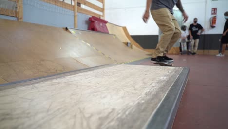 Toma-En-ángulo-Bajo-De-Un-Patinador-Masculino-Saltando-Sobre-Una-Pequeña-Rampa-De-Madera-Y-Deslizándose