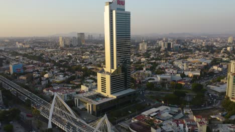 Drone-Flies-Towards-Riu-Hotel-Skyscraper,-Gradual-Pan-Right-Reveals-Guadalajara