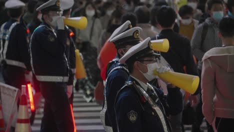 Gruppe-Von-Polizisten,-Die-Gelbe-Megaphone-Verwenden,-Während-Sie-Die-Menge-An-Der-Shibuya-kreuzung-In-Der-Halloween-nacht-2020-Kontrollieren---Mittlere-Aufnahme