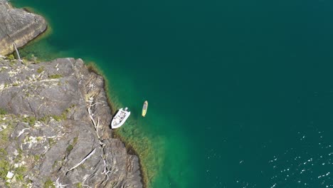 Aerial-top-down-of-a-man-in-a-kayak-near-a-rocky-shore-in-turquoise-water-Puelo-Lake,-Patagonia-Argentina