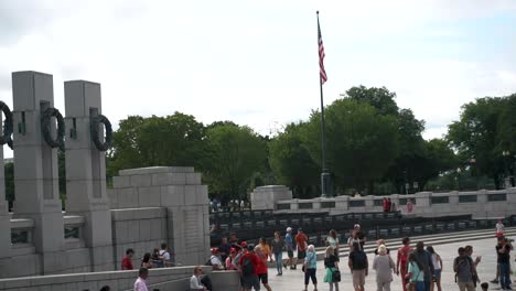 Pillars-And-US-Flag-At-World-War-II-Memorial-In-Washington-DC-With-People-Walking-At-Daytime---high-angle,-wide-shot