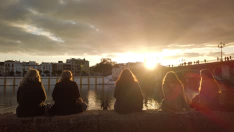 Frauen-Sitzen-Und-Beobachten-Den-Atemberaubenden-Goldenen-Sonnenuntergang-über-Dem-Fluss-In-Spanien