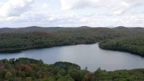 Idyllic-lake-surrounded-by-a-thick-wilderness-forest-in-autumn---aerial-pull-back-view