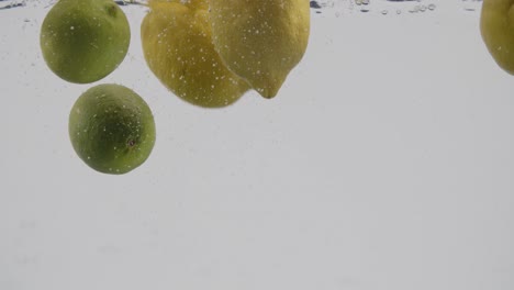 Ganze-Zitronen-Und-Limetten,-Die-In-Wasser-Spritzen