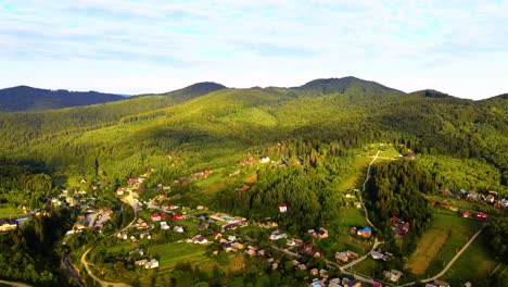Aerial-view-overlooking-a-village,-in-middle-of-sunlit-forest-and-hills,-golden-hour,-in-the-Carpathian-Mountains,-Ukraine---dolly,-drone-shot