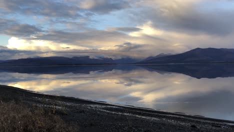 Kluane-lake-in-Canada-at-cloudy-reflective-sunset,-rising-drone-shot
