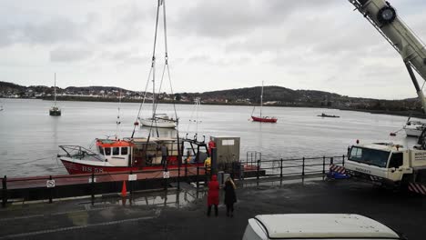 Hydraulic-crane-vehicle-lifting-fishing-boat-on-Conwy-Wales-harbour-waterfront