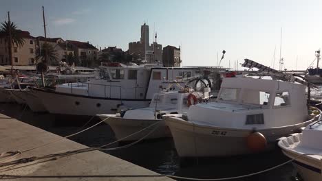 Panning-view-of-boats-docked-at-Komiza,-on-the-island-of-Vis-in-Croatia,-with-Komiza-Castle-in-the-background