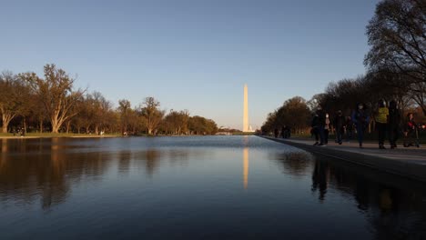 Zeitrafferansicht-Von-Menschenmassen,-Die-Neben-Dem-Reflektierenden-Pool-In-Washington,-DC,-USA,-Mit-Dem-Washington-Monument-In-Der-Ferne-Und-Spiegelung-In-Ruhigem-Wasser-Spazieren-Gehen