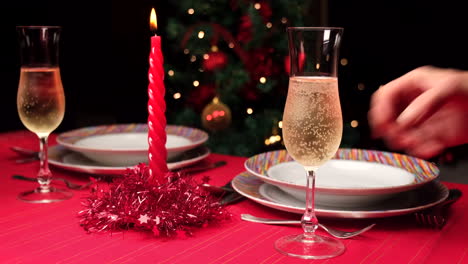 Die-Hand-Der-Frau,-Die-Champagnerflöte-Auf-Den-Roten-Tisch-Setzt,-Der-Für-Weihnachten-In-Zeitlupe-Eingestellt-Wird