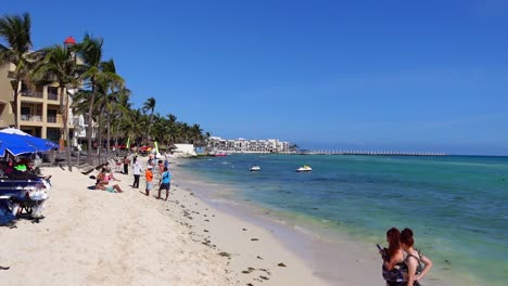 Schwenken-Nach-Links,-Malerische-Ansicht-Des-Strandes-An-Einem-Sonnigen-In-Yucatan,-Mexiko,-Menschen,-Die-Sich-Um-Das-Strandufer-Im-Hintergrund-Versammeln