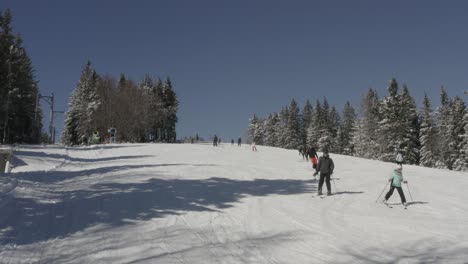 Kope-ski-resort-with-skier-families-going-downhill-near-snow-machines,-Aerial-pedestal-rising-shot