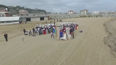 Aerial-view-of-romantic-beach-wedding-with-guests-holding-white-balloons,-Spain