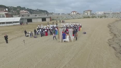 Vista-Aérea-De-Una-Boda-Romántica-En-La-Playa-Con-Invitados-Con-Globos-Blancos,-España