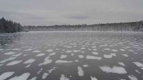 Aerial-flight-over-frozen-lake-with-fresh-snowfall-surrounded-by-forestry