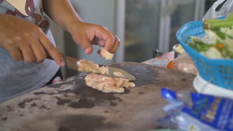 Lady-slicing-fresh-chicken-breast-on-a-cutting-board-in-her-kitchen