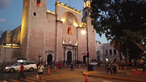 Showing-crowds-of-people-crossing-roads-at-dusk-in-front-of-the-Catedral-de-San-Ildefonso,-Merida,-Yacatan,-Mexico