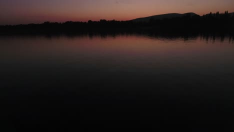 Tilt-up-motion-shot-over-water,-revealing-the-sunset-or-sunrise