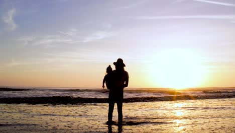 Eine-Frau-Genießt-Den-Sonnenuntergang-Am-Strand-In-4k-Mit-Ihrem-Kind-Und-Dem-Wunderschönen-Sonnenuntergang-Als-Hintergrund