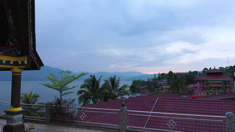 Drone-footage-of-a-woman-walking-across-a-tiled-roof-at-sunrise-at-a-waterfront-resort-on-Lake-Toba-in-North-Sumatra,-Indonesia