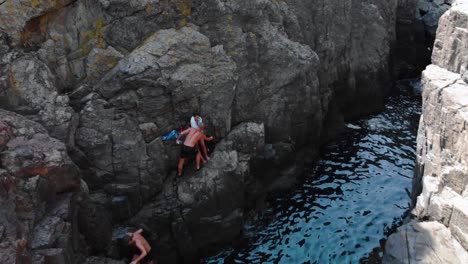 Aerial-shot-of-two-boys-and-girl-on-high-seashore-cliffs-after-diving,-summer-time