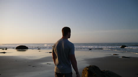 Ein-Starker-Mann,-Der-Die-Meereswellen-Beobachtet-Und-Sich-Für-Einen-Morgendlichen-Lauf-Und-Ein-Training-Am-Strand-Bei-Sonnenaufgang-In-Santa-Barbara,-Kalifornien,-Zeitlupe-Ausdehnt