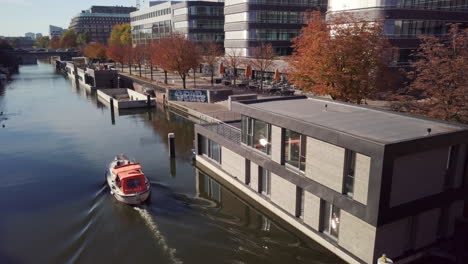 Motorboat-is-slowly-cruising-down-the-channel-on-a-sunny-afternoon-and-passing-by-a-houseboat-estate