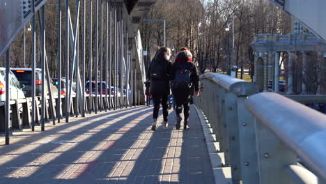Ein-Paar-Mädchen-Gehen-über-Die-Mindaugas-Brücke,-Gekleidet-In-Warme-Winterkleidung-In-Dunkler-Farbe