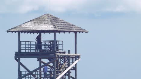 Distant-view-of-young-people-climbing-up-in-lake-Liepaja-birdwatching-tower-in-sunny-summer-day,-medium-shot-from-a-distance