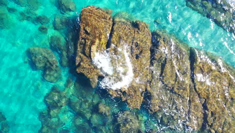 static-shot-of-mediterranean-sea-with-big-rock-breaking-the-surface-of-crystal-clear-water,-interesting-pretty-4k-shot-of-tropical-water