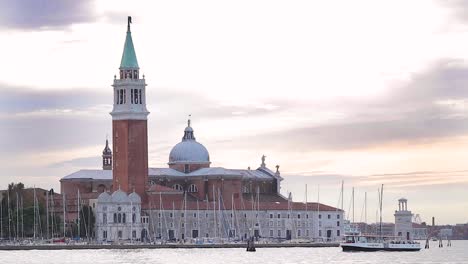 wide-shoot-of-boats-passing-by-church-of-San-Giorgio-Maggiore-in-Venice,-Italy-at-sunset