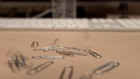 A-hand-full-of-paper-clips-slowly-dropping-onto-an-office-desk-a-little-bit-at-a-time