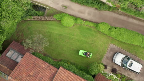 Static-Aerial-Shot-of-Man-Mowing-Lawn-of-Home-on-Summer’s-Day-using-Ride-On-Lawnmower-from-Birds-Eye-View-Perspective