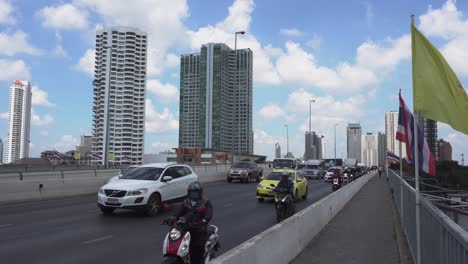 Tráfico-En-La-Concurrida-Ciudad-De-Bangkok-Con-Bandera-Nacional-En-El-Puente,-Tailandia