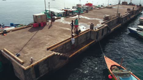 Drohnenaufnahmen-Einer-Frau,-Die-Auf-Dem-örtlichen-Fischmarkt-Auf-Dem-Steg-Steht,-Während-Kinder-Im-Hintergrund-Spielen