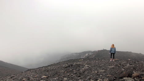 Female-Walking-Along-Crater-Of-Mt-Etna-With-Clouds-Rolling-In-Background