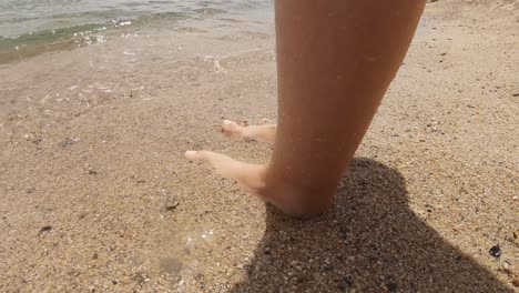 Eine-Frau,-Die-Am-Meer-An-Einem-Sandstrand-Steht,-Während-Die-Wellen-Langsam-Ihre-Füße-Berühren