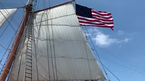 Close-up-of-a-large-white-sail-with-the-American-flag-waving-in-the-background