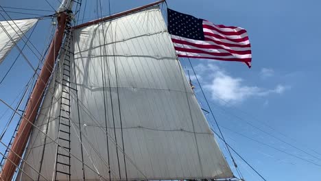 Primer-Plano-De-Una-Gran-Vela-Blanca-Con-La-Bandera-Americana-Ondeando-En-El-Fondo