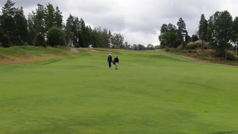 Golf-players-walking-pass-the-golf-course-in-Sweden,-aerial-orbit-view