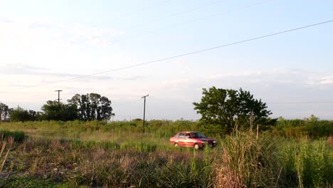 A-red-80'-Fiat-Duna-moves-left-to-right-through-a-rural-road-late-in-the-afternoon